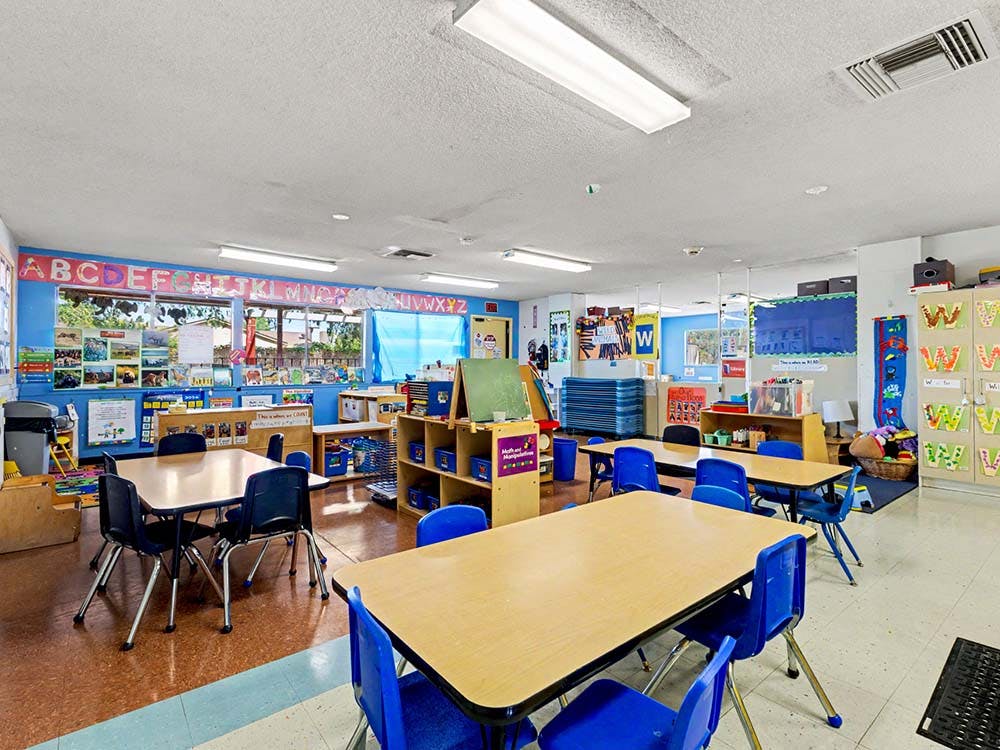 Empty classroom with small tables and chairs, ABCs above windows
