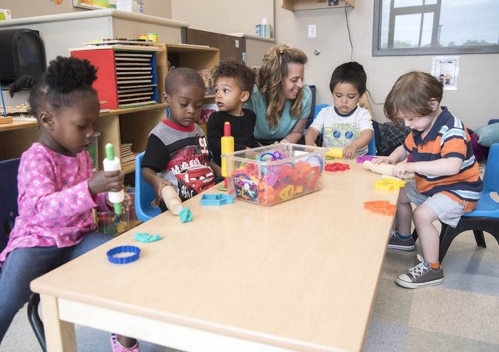 Adult and children playing with modeling clay at a table in a classroom