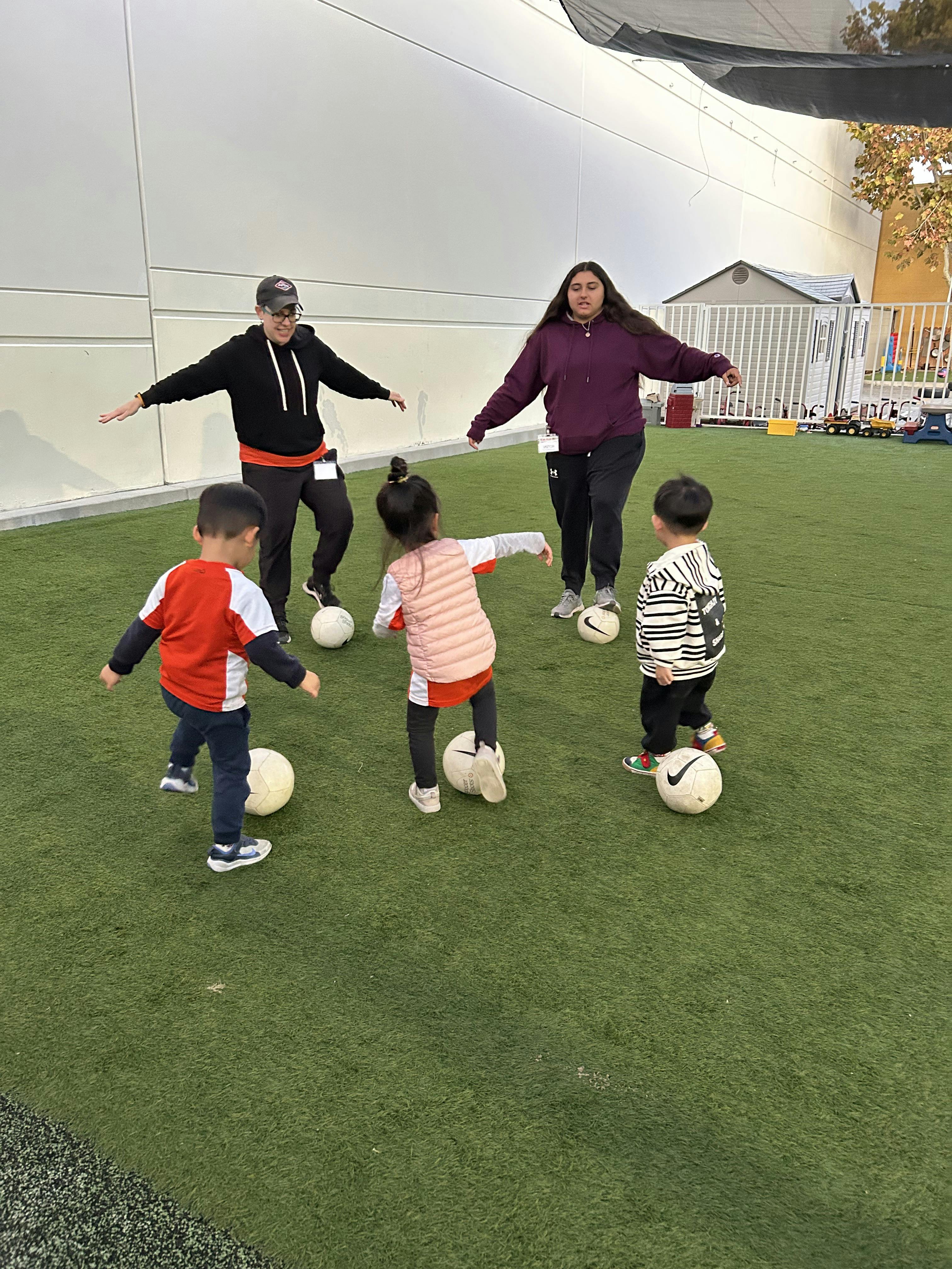 Adults leading children in a soccer drill on a turf field