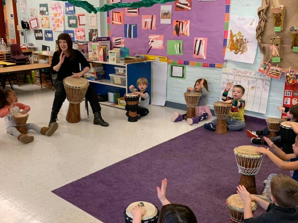 Person playing a drum with children in a classroom