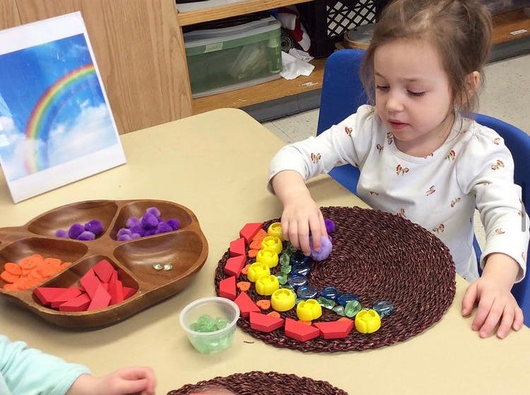 Child arranging colorful objects on a mat at a table