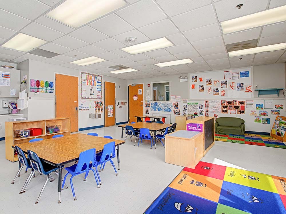 Empty classroom with small tables and chairs, whiteboards, and children's artwork