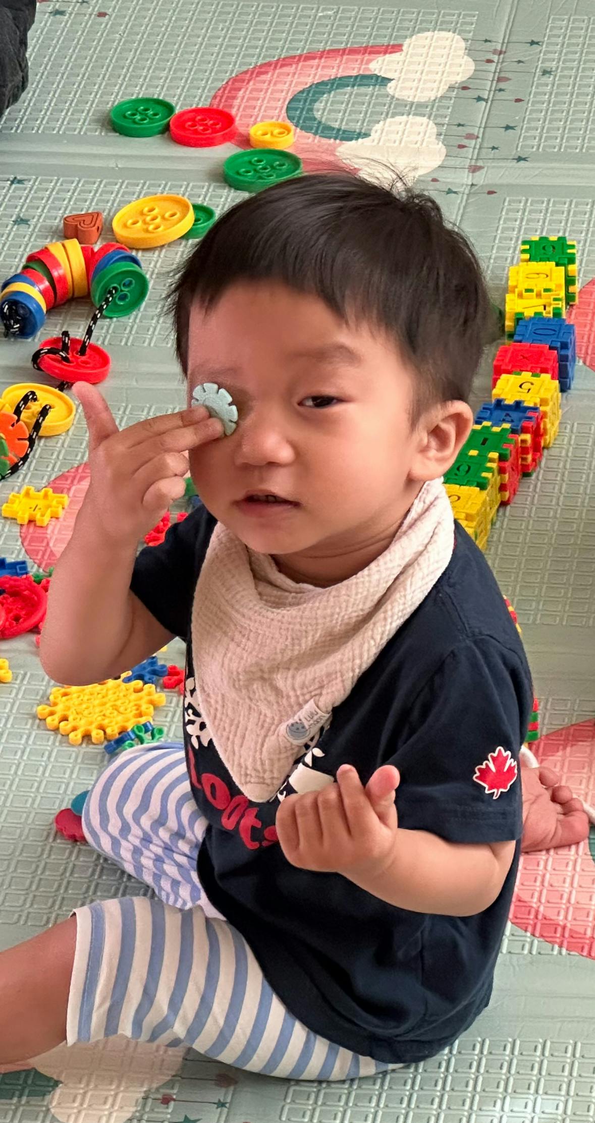 Child sitting on floor with toy piece over one eye