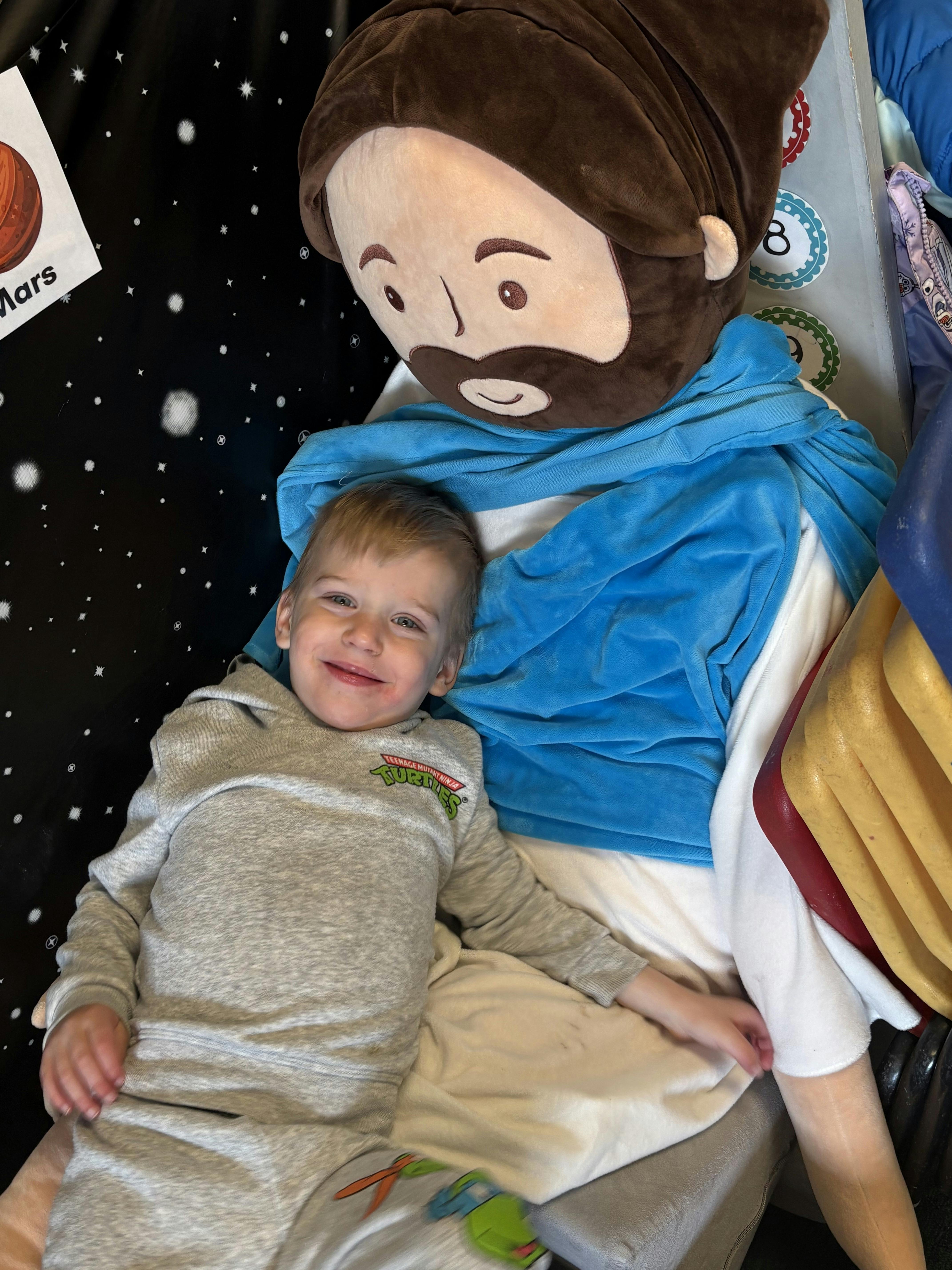 Child smiling while laying next to a large plush doll