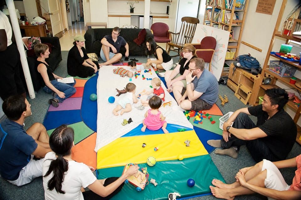 Adults and children sitting on the floor around a play mat