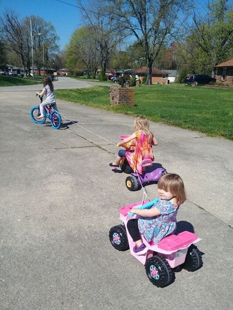 Three children riding on a street, one on a bicycle and two on toy vehicles