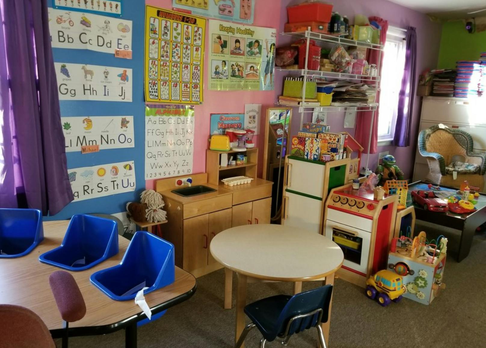 Classroom with small tables and chairs, play kitchen, and alphabet charts