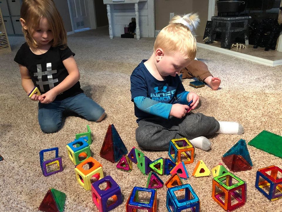 Two children playing with colorful magnetic building blocks on a carpet