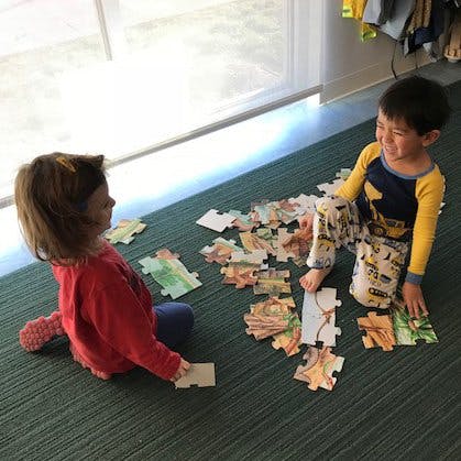 Two children sitting on a rug playing with puzzle pieces