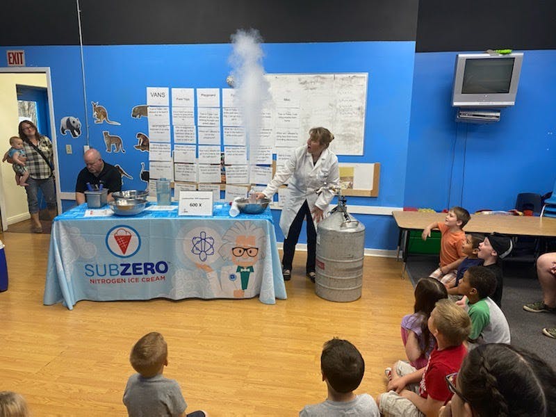 Person in lab coat demonstrating science experiment with smoke to children
