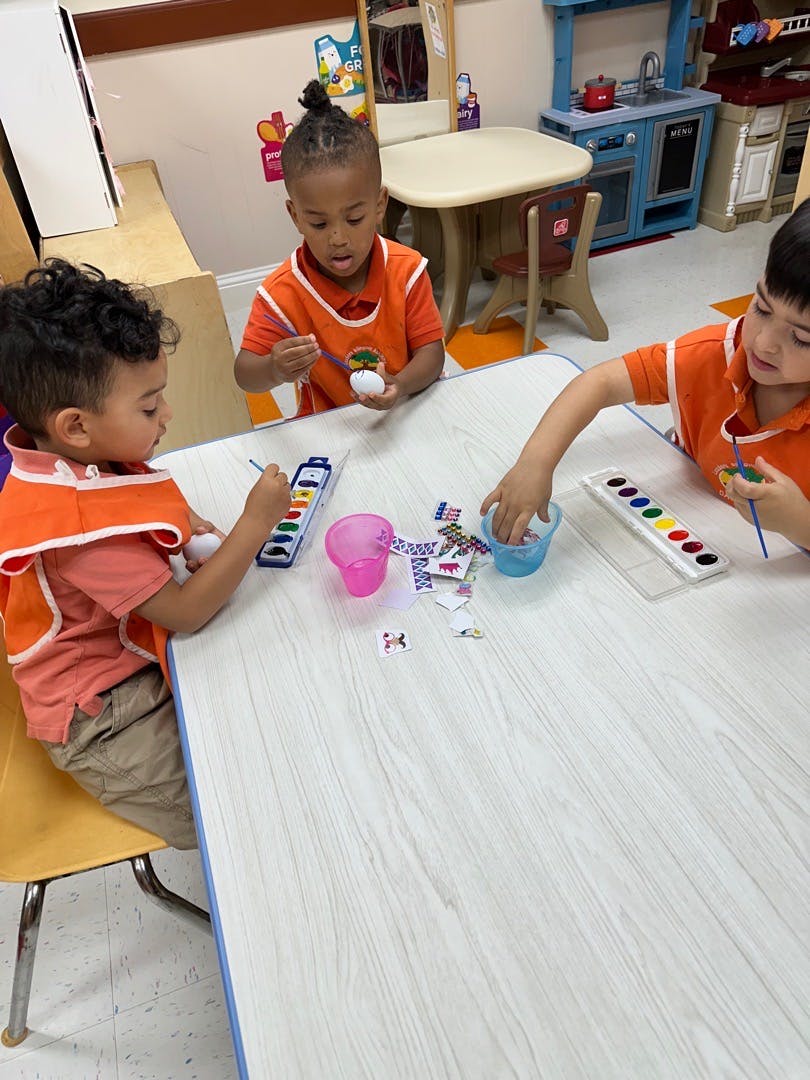 Three children painting at a table in a classroom