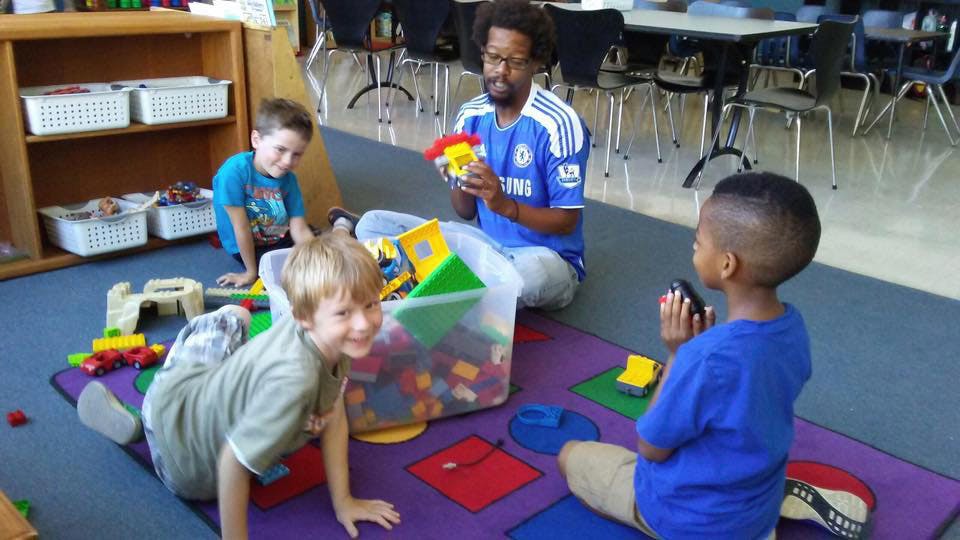 Adult and three children playing with toys on a rug in a classroom