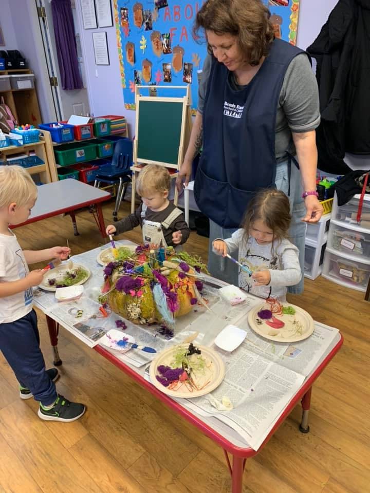 Adult and three children decorating a pumpkin with colorful craft supplies