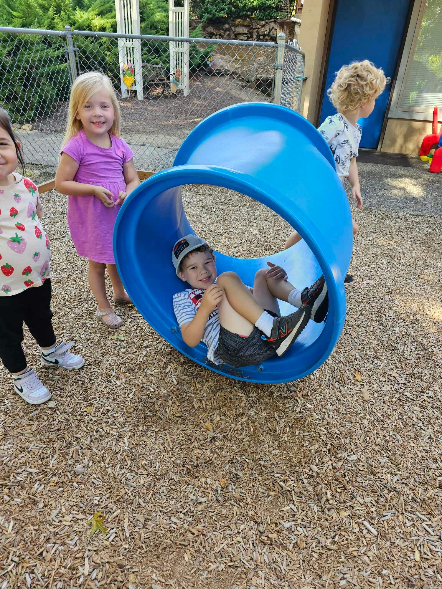 Child in a blue tunnel slide on a playground with other children nearby