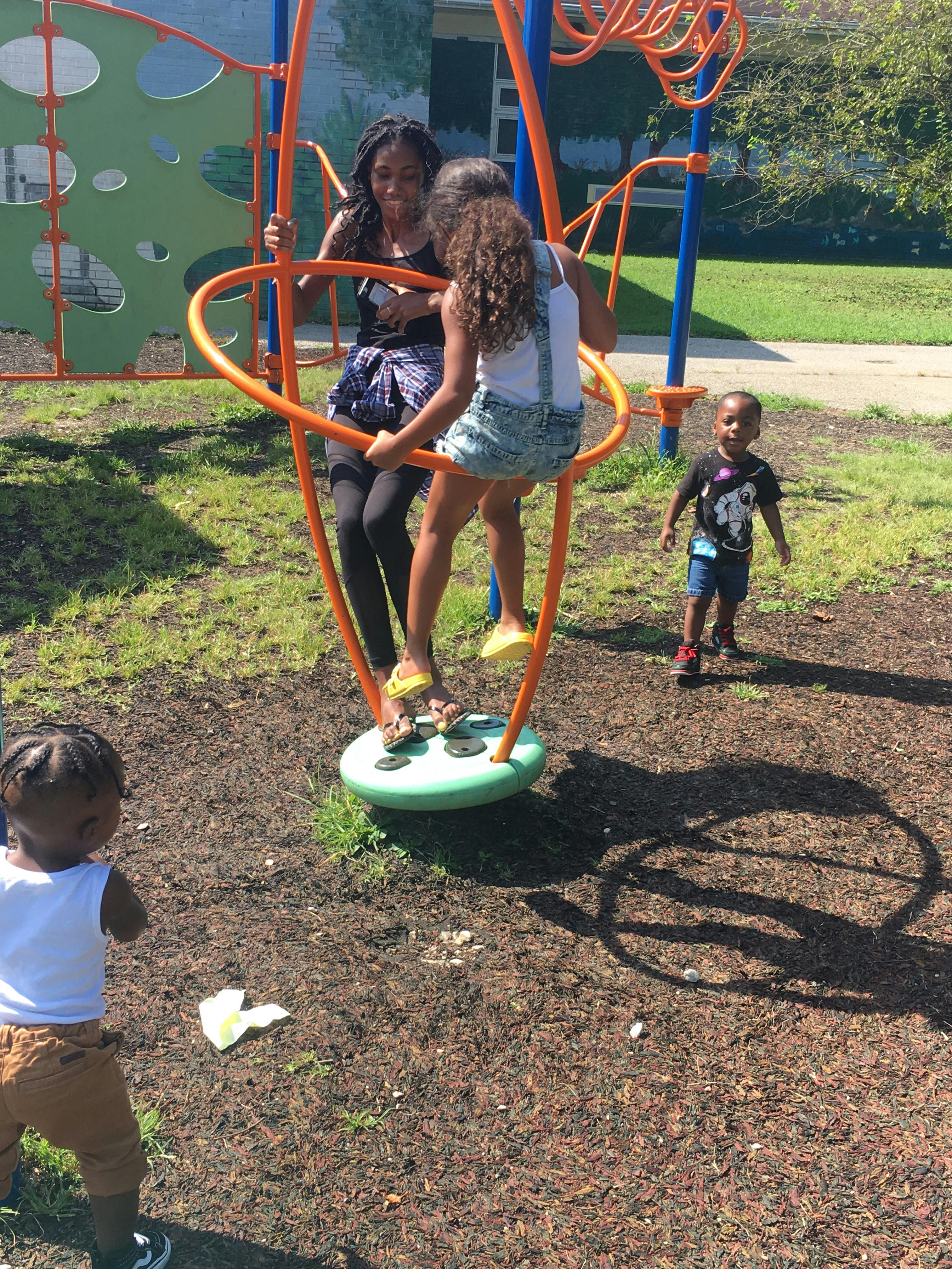 Two children on a playground spinner, with two other children nearby