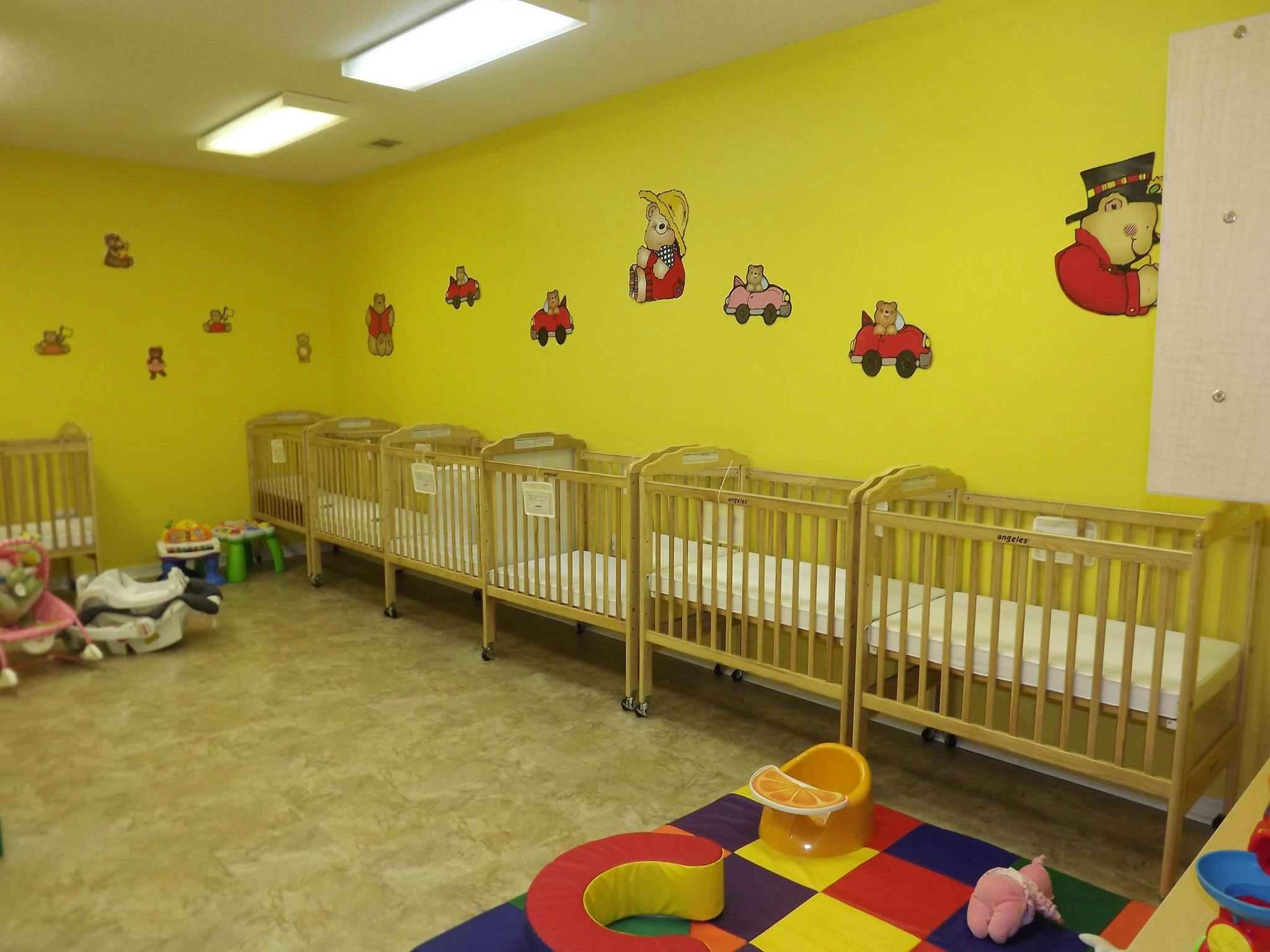 Row of cribs in a room with yellow walls and cartoon decals