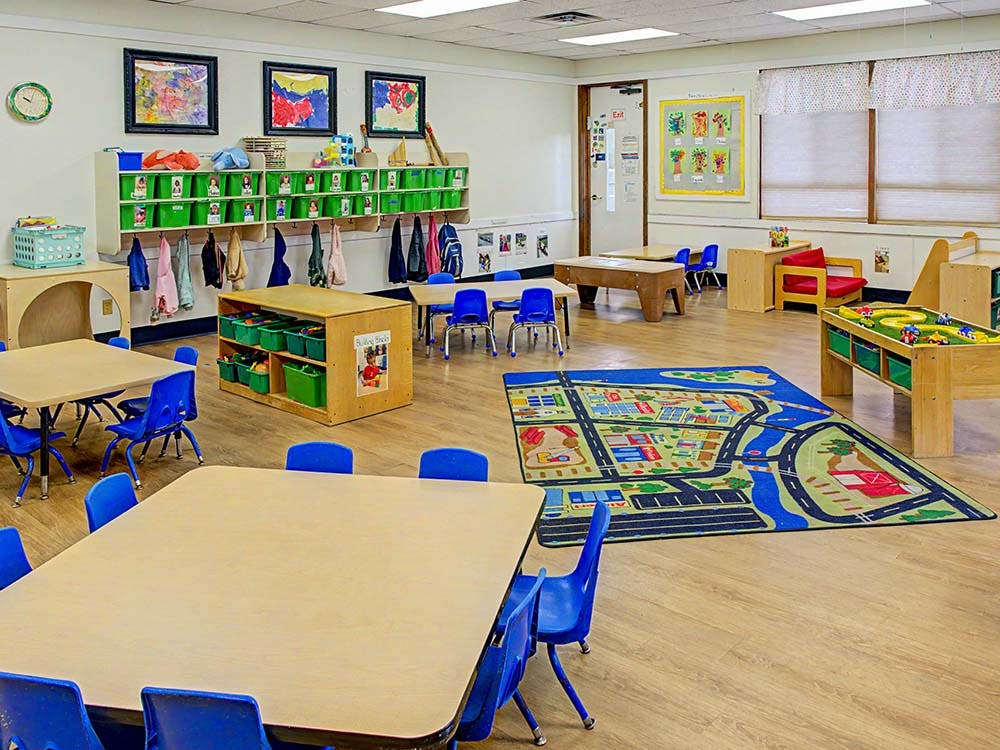 Empty classroom with small tables and chairs, storage, and play rug
