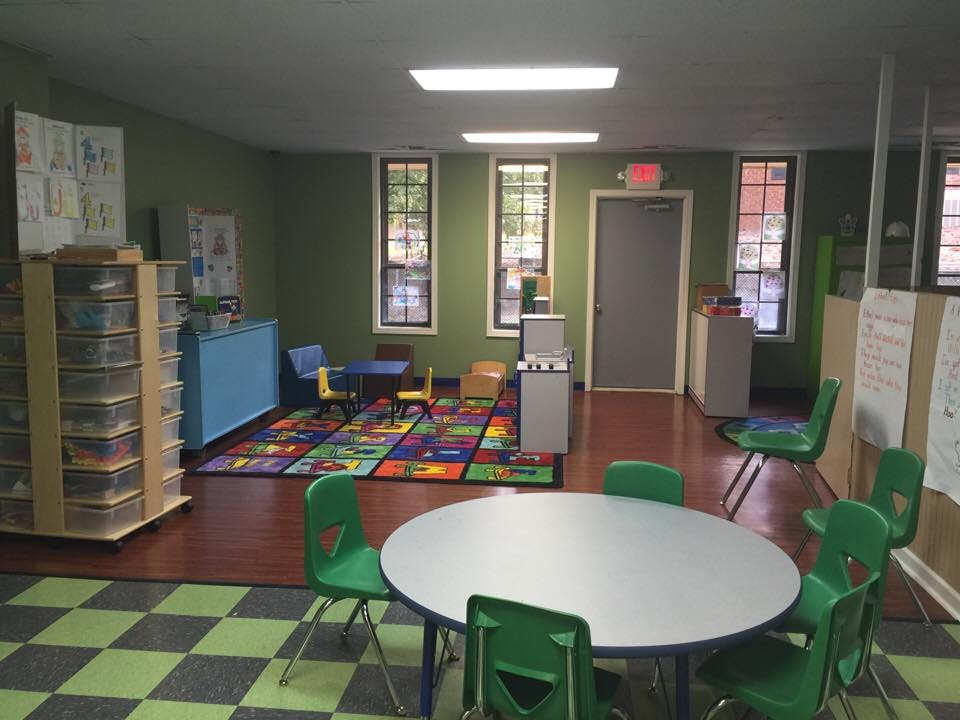 Classroom with small tables and chairs, colorful rug, and storage shelves