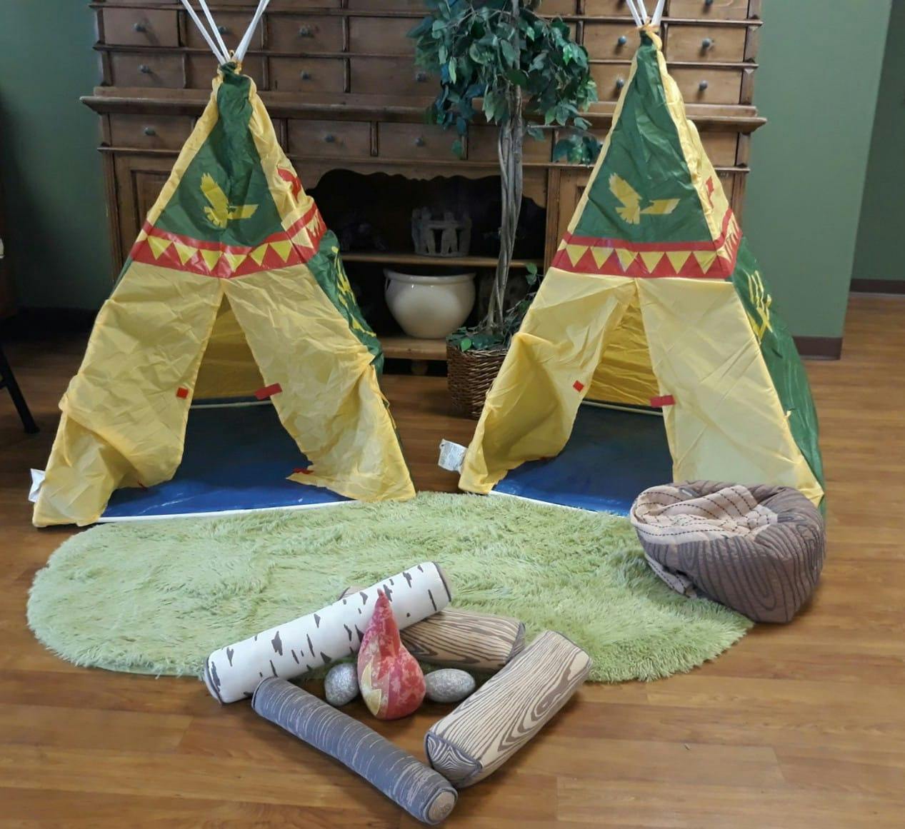 Two play teepees with a green rug and toy logs