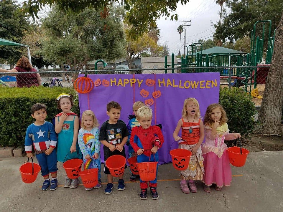 Children in costumes holding buckets in front of a "Happy Halloween" banner
