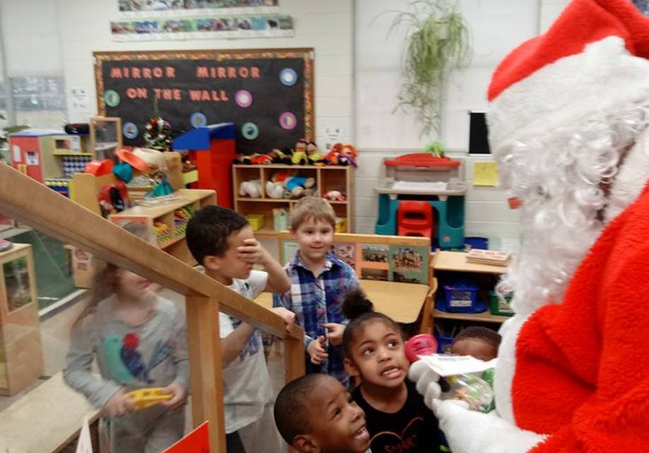 Person dressed as Santa Claus interacting with children in a classroom