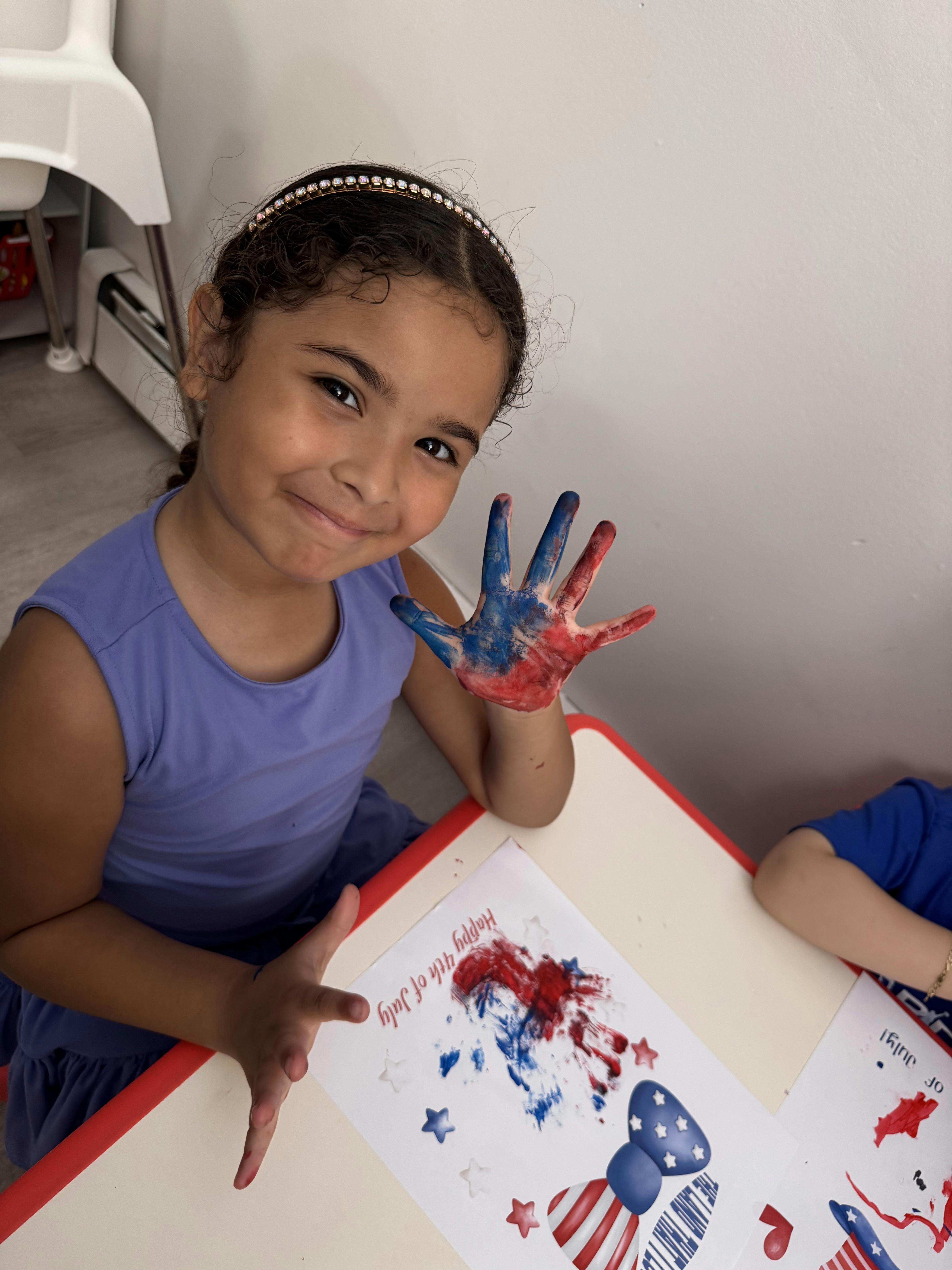 Child showing a hand covered in red and blue paint over a holiday craft project
