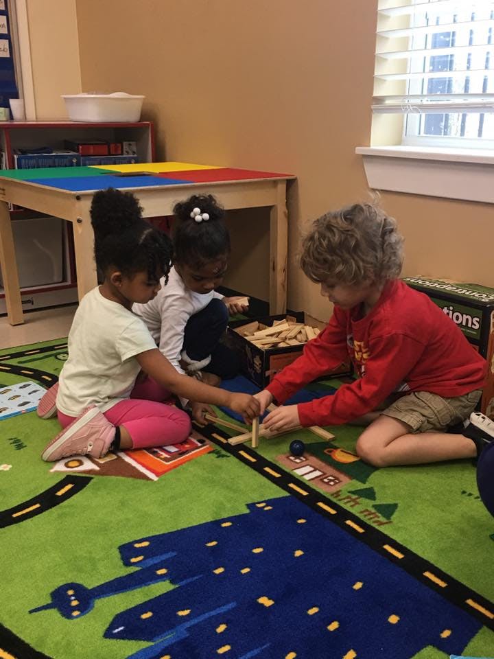 Three children playing with wooden blocks on a rug