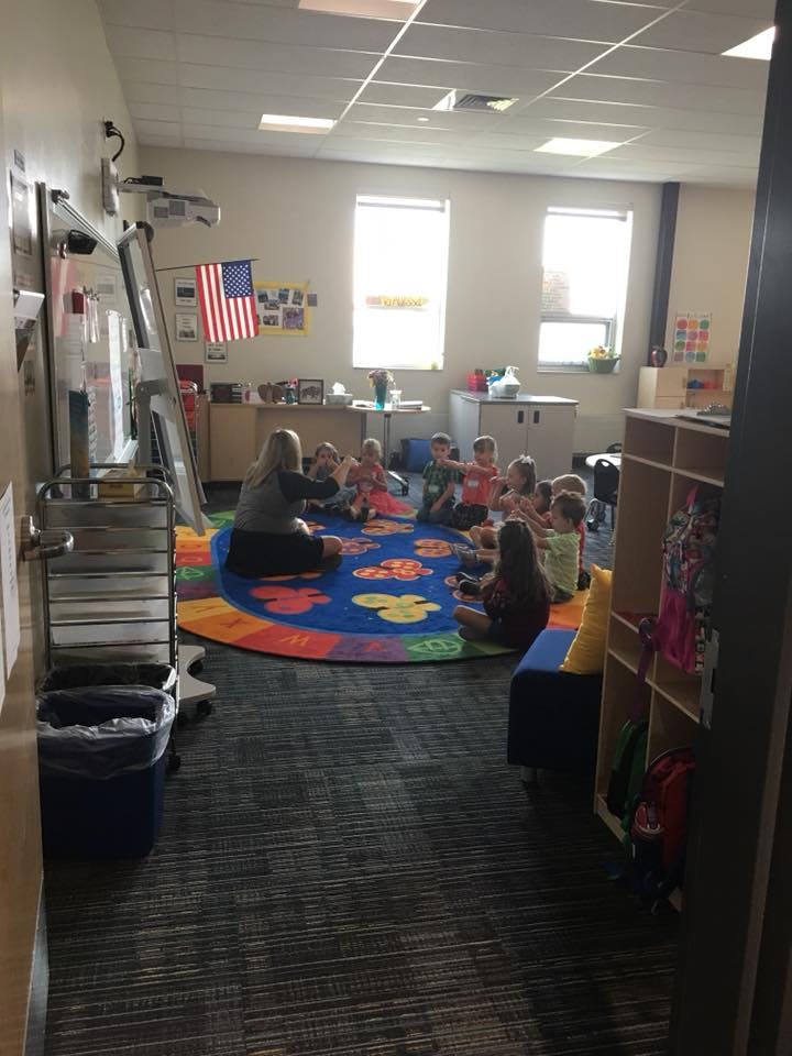 Adult and children sitting on a colorful rug in a classroom