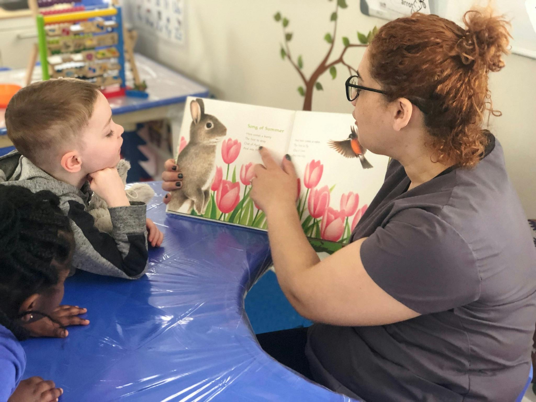 Person reading a book with a rabbit illustration to two children