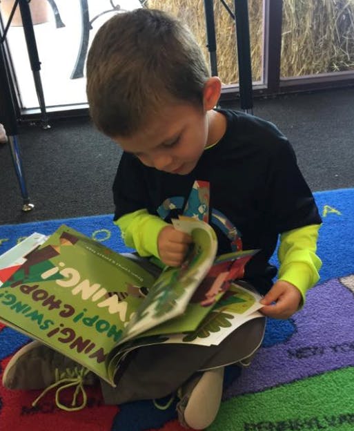Child sitting on floor, looking at a book with text "WING! HOP! SWING!"