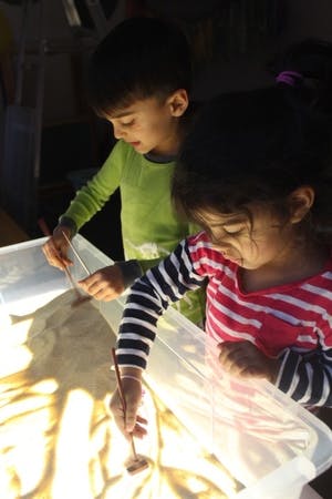 Two children drawing in sand on a light table