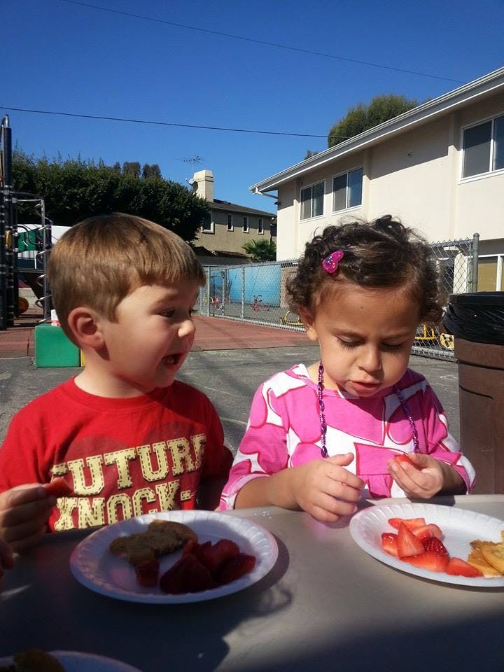 Two children eating snacks at a table outdoors