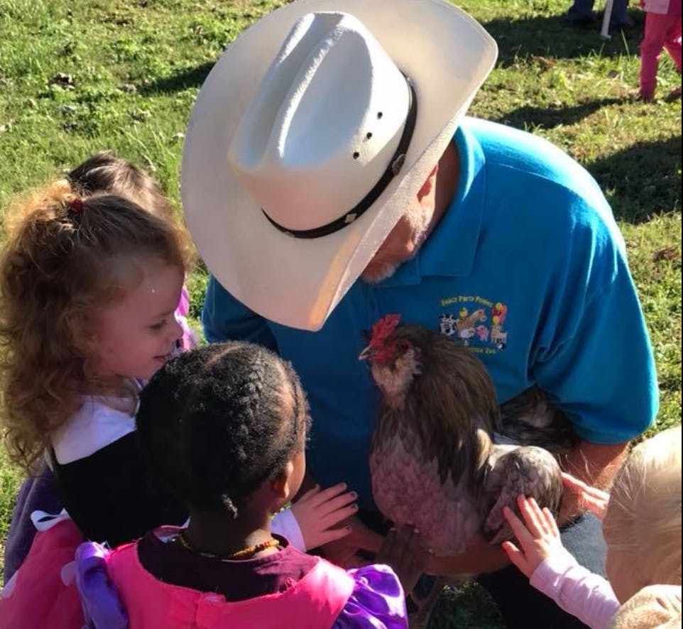 Person in cowboy hat holding a chicken for children to see