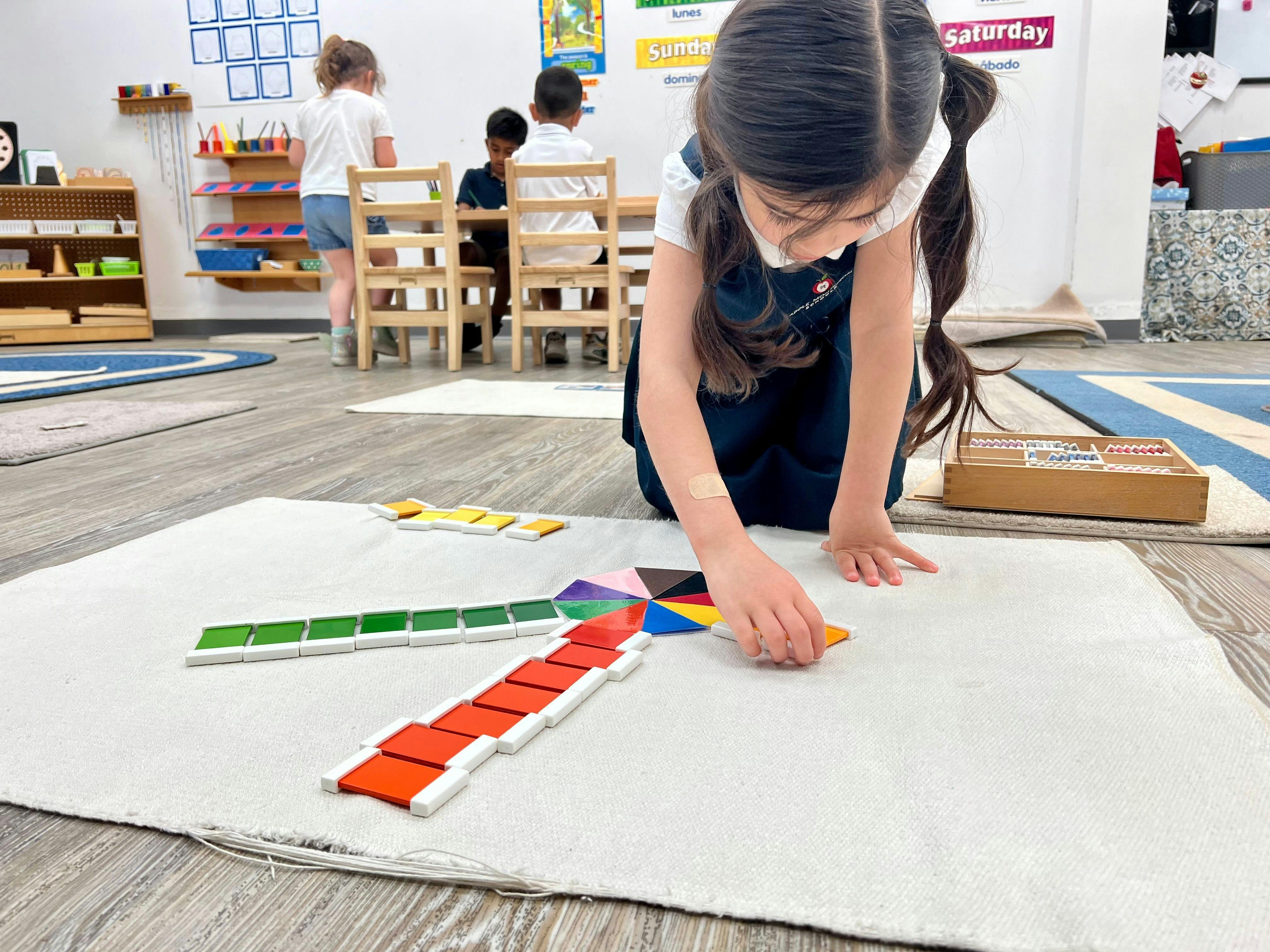 Child playing with colorful geometric shapes on a white mat in a classroom