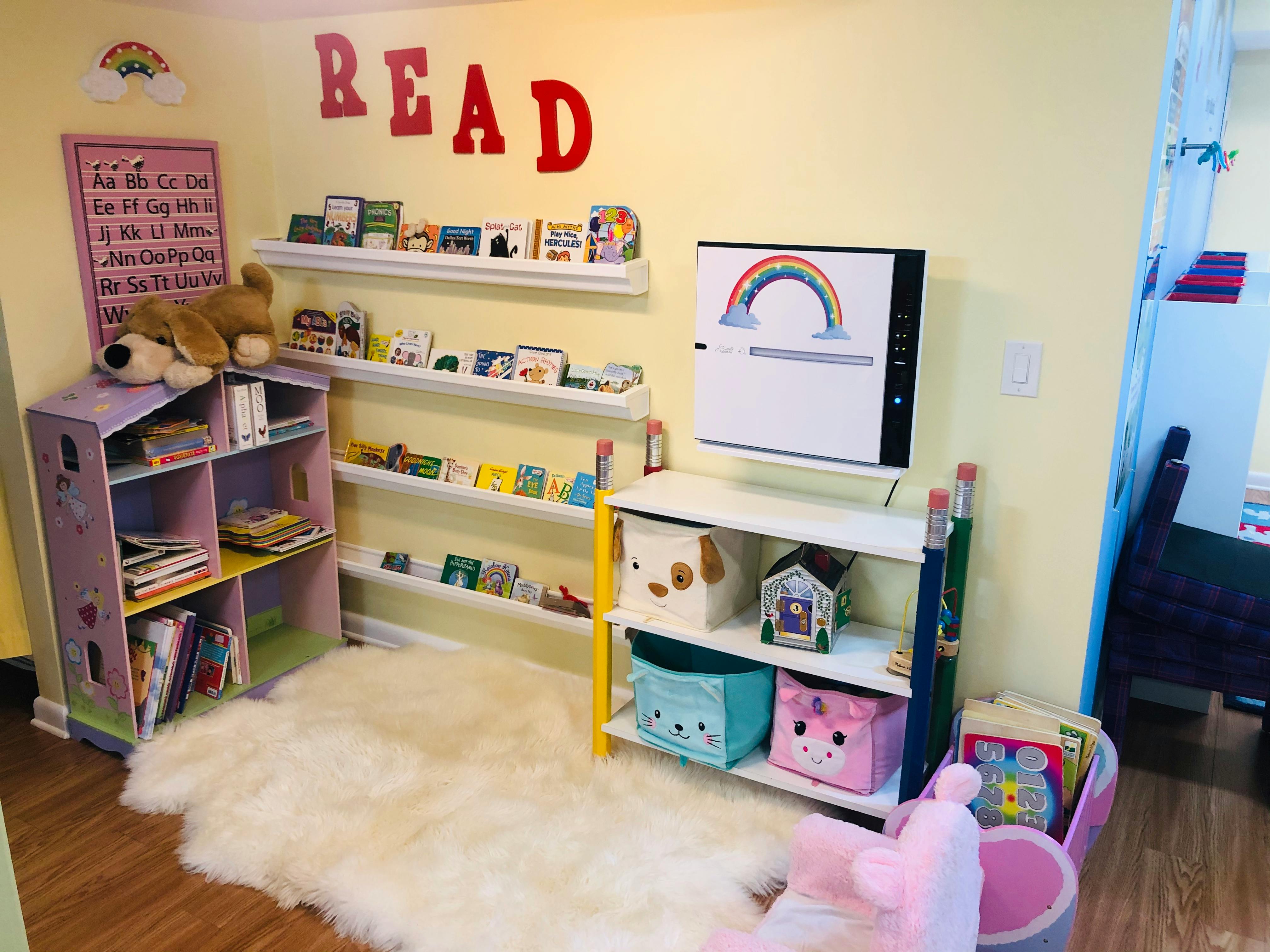 Children's reading nook with bookshelves, a rug, and a screen displaying a rainbow