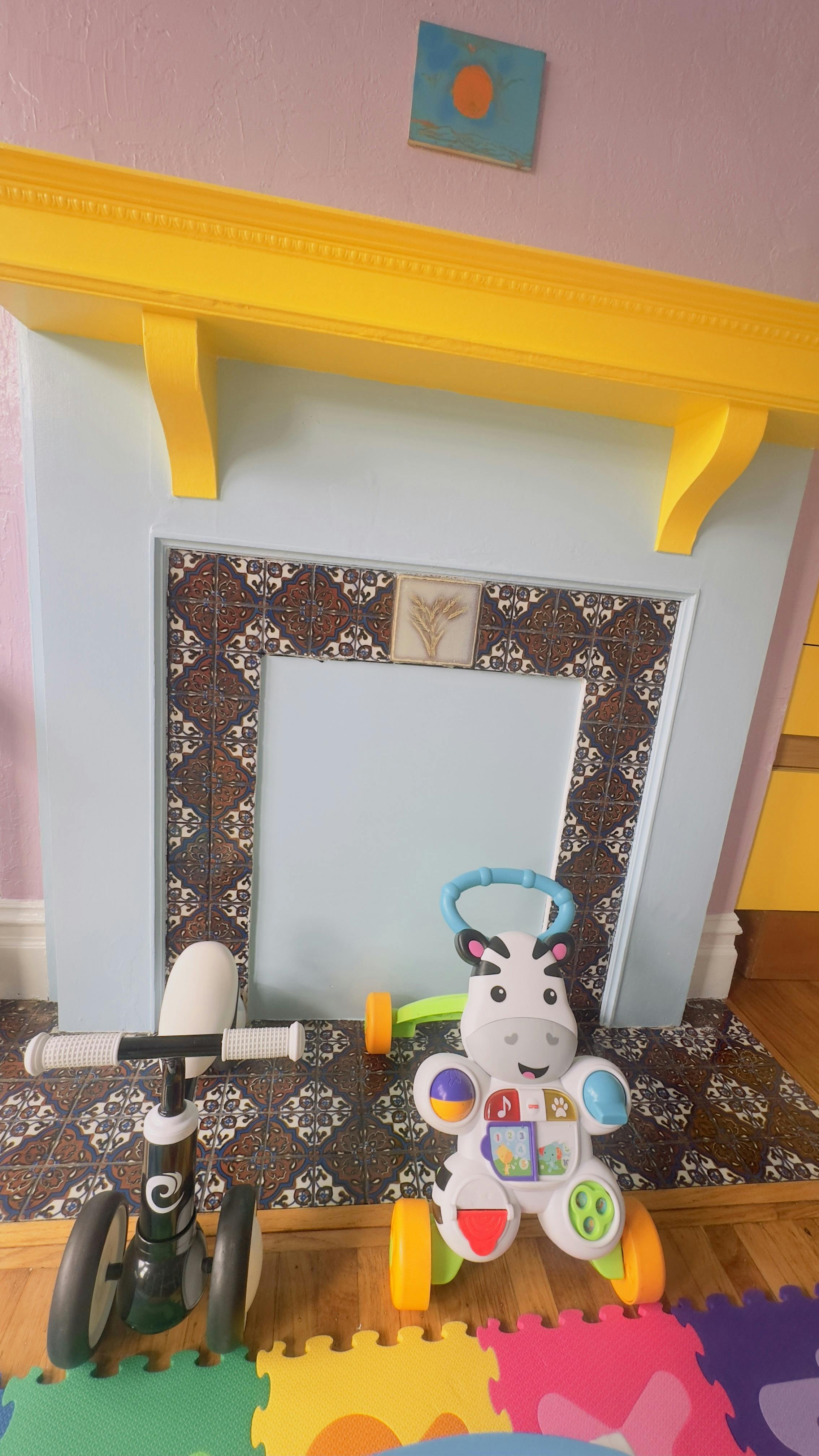 Child's tricycle and a zebra-shaped baby walker toy in front of a fireplace