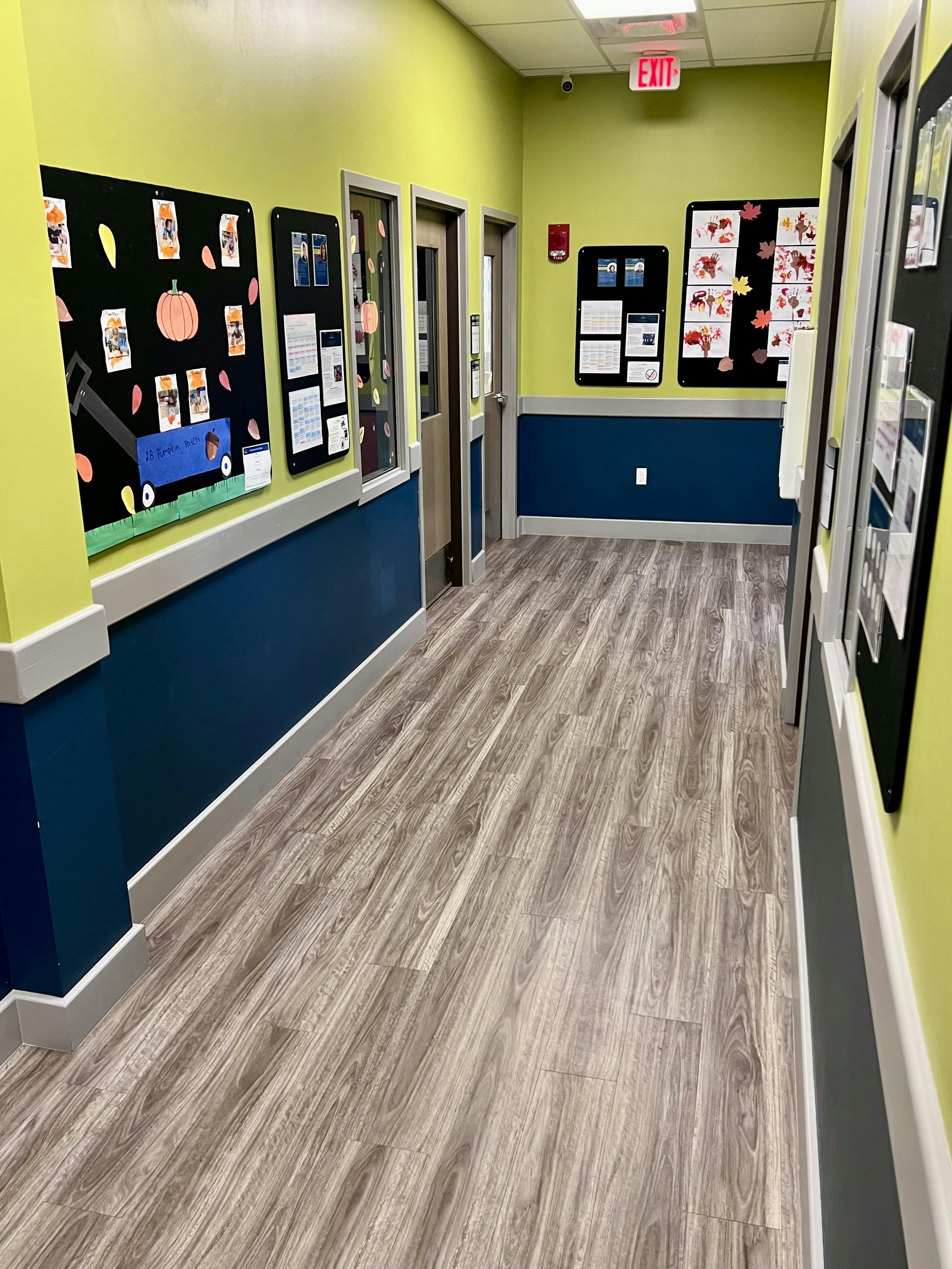 Hallway with light green walls, blue wainscoting, and bulletin boards