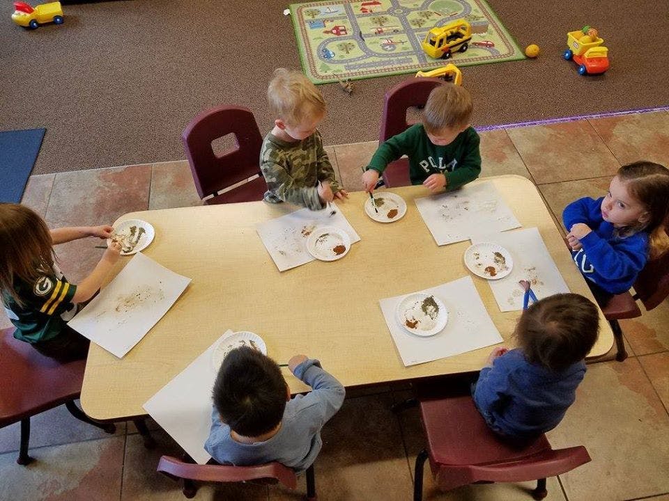 Children sitting at a table with plates and papers