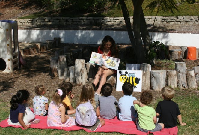 Person reading a book to a group of children outdoors