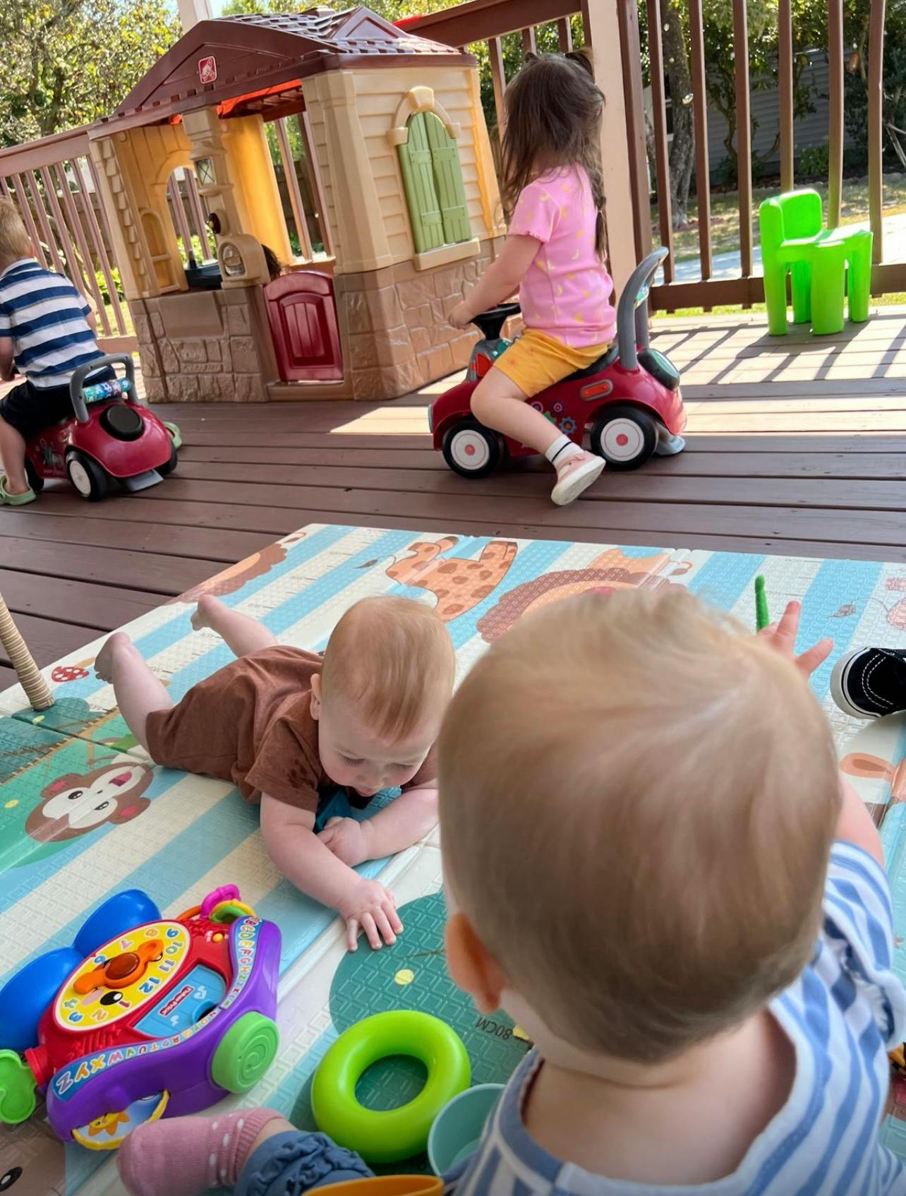 Two children on ride-on toys and two babies playing on a mat outdoors