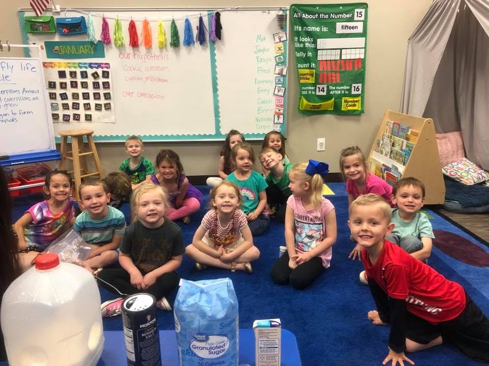 Group of children sitting on a blue rug in a classroom