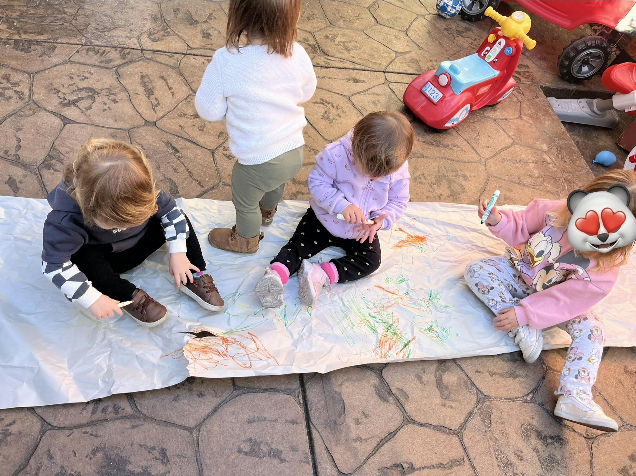 Three children drawing on a large sheet of paper outdoors