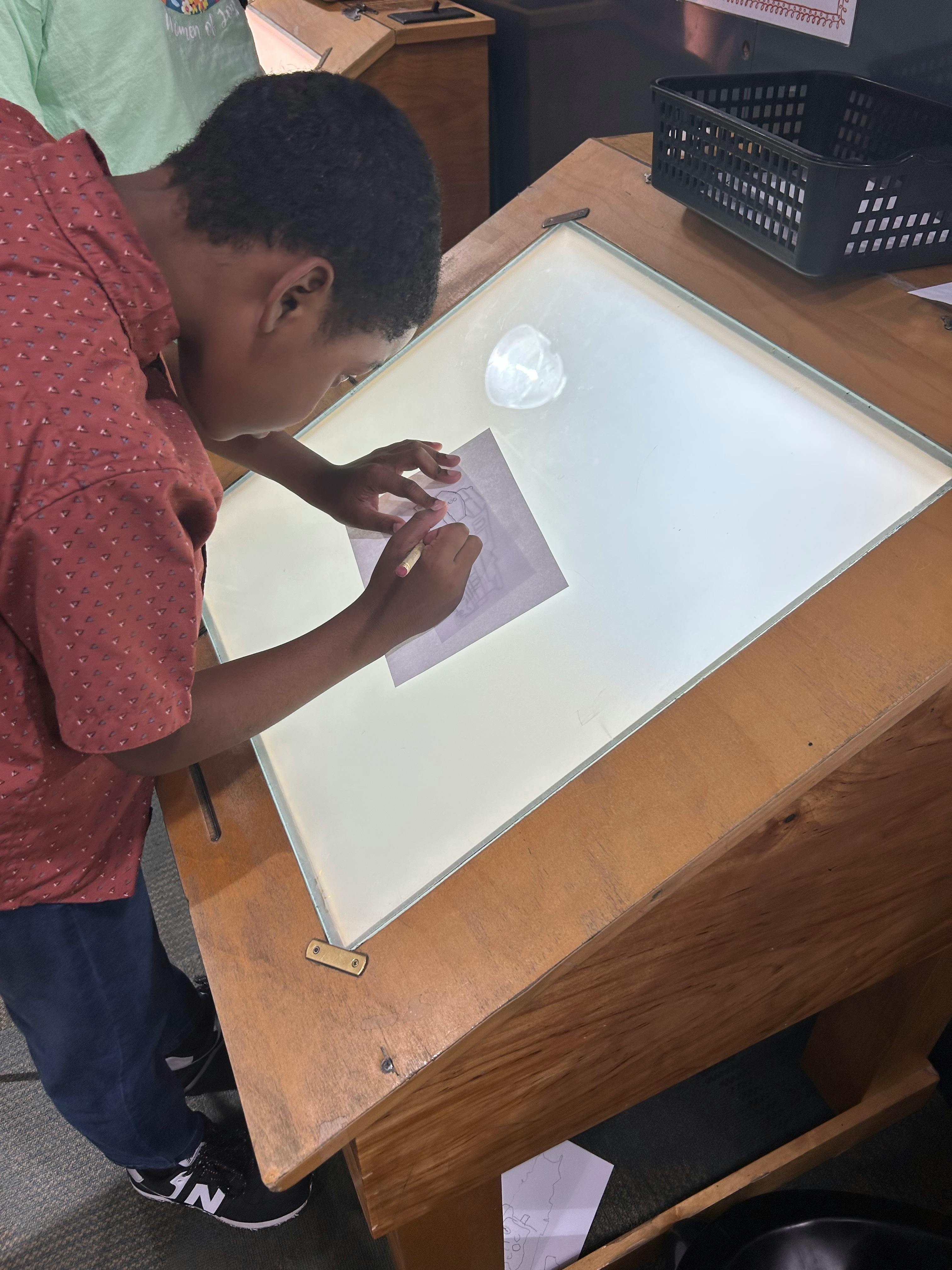 Person drawing on paper on a light table