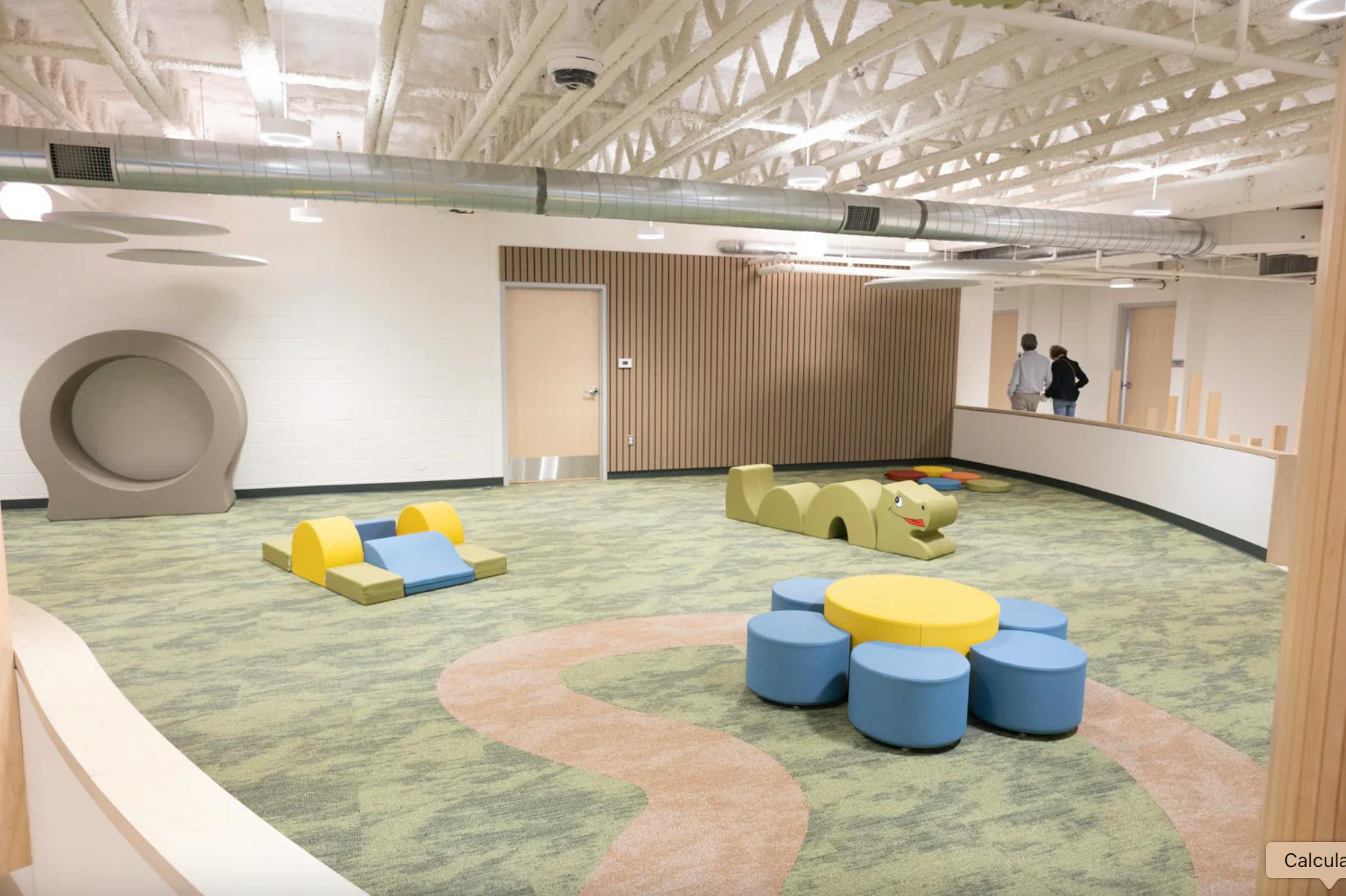 Indoor play area with soft play equipment and two people in background