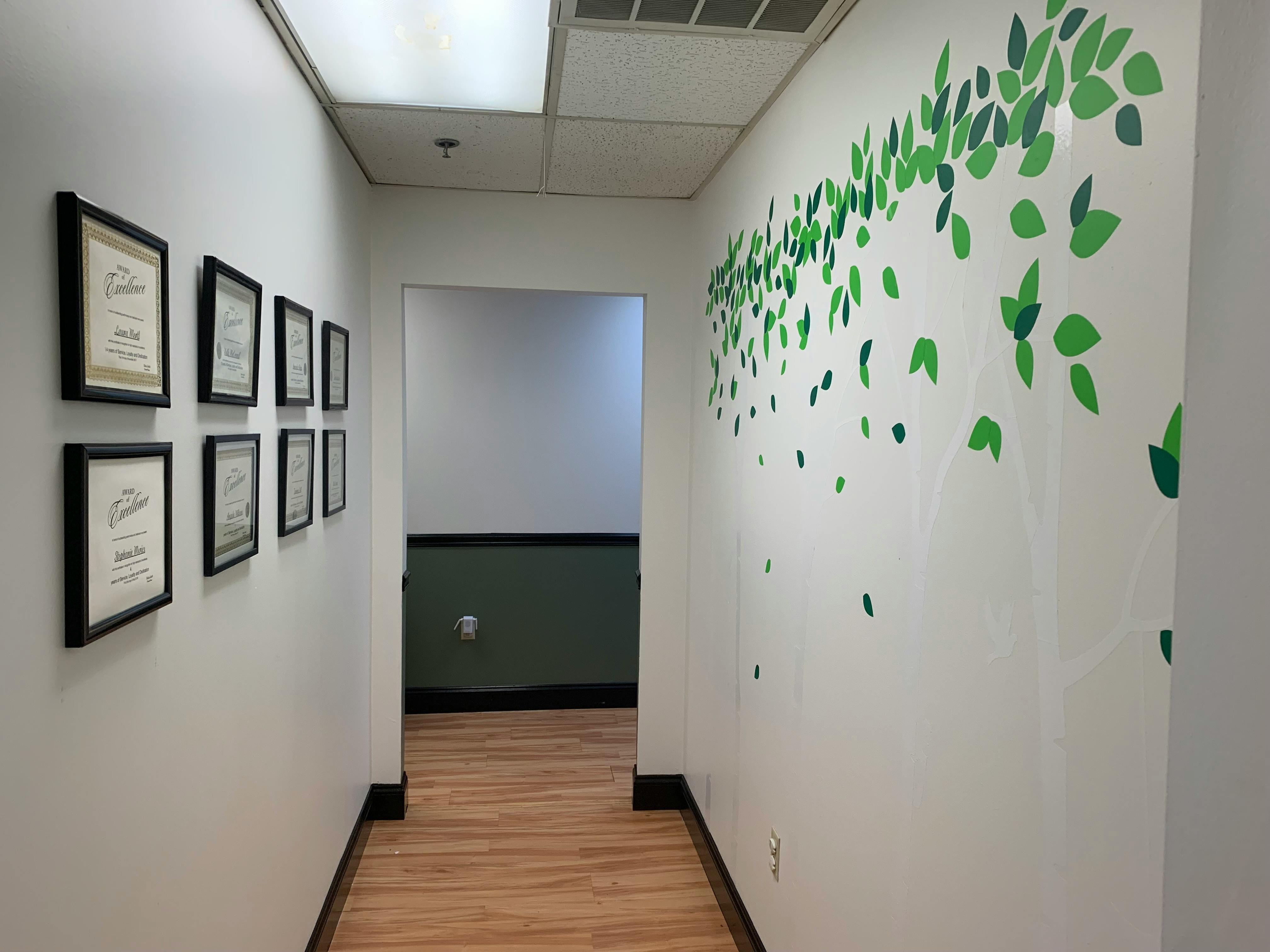 Hallway with framed documents on one wall and green leaf decals on the other