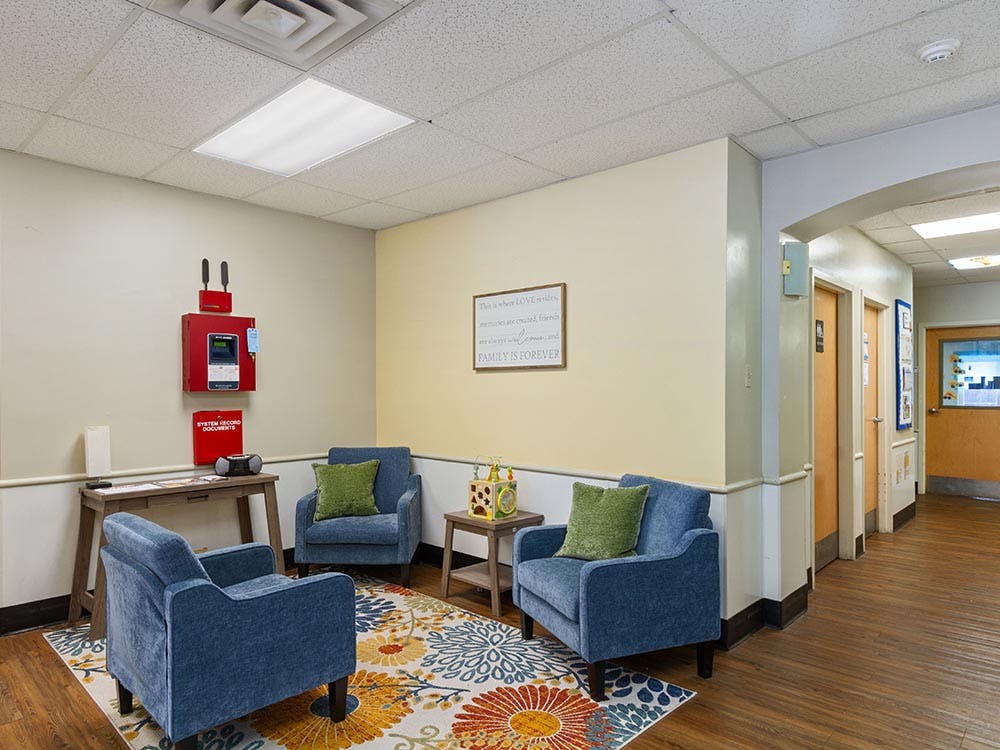 Lounge area with three blue armchairs on a floral rug, with a hallway to the right