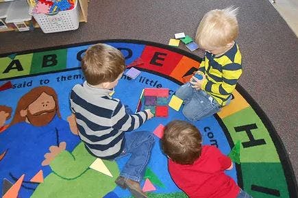 Three children playing with blocks on a colorful alphabet rug