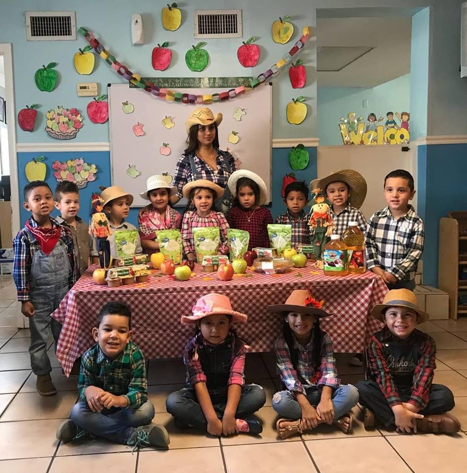 Adult and children in cowboy hats and plaid shirts around a table with apples