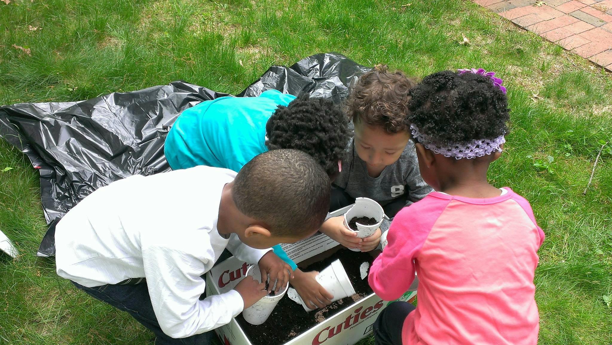 Four children planting in a garden box outdoors
