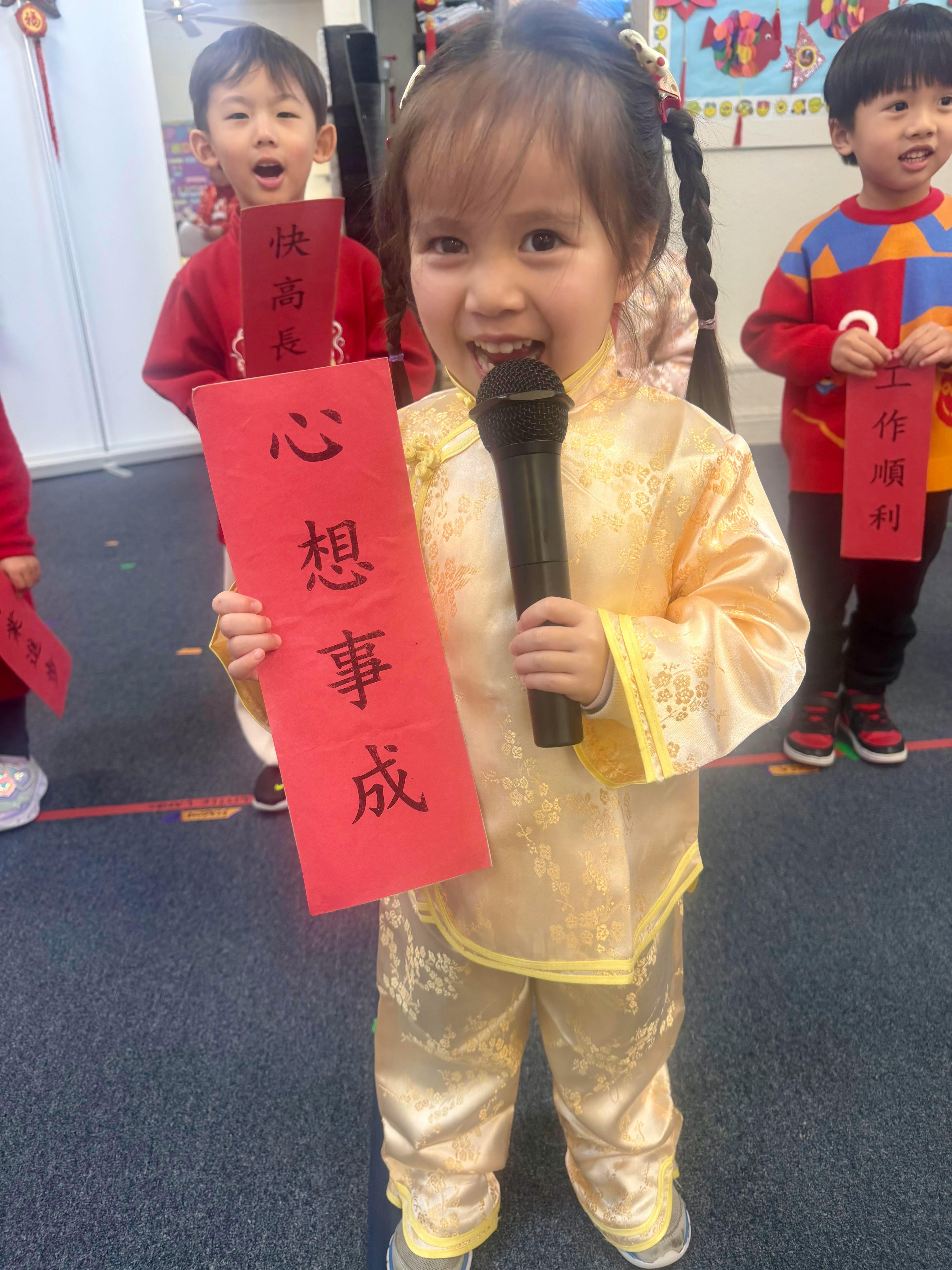 Child wearing traditional clothing holding a microphone and a red banner